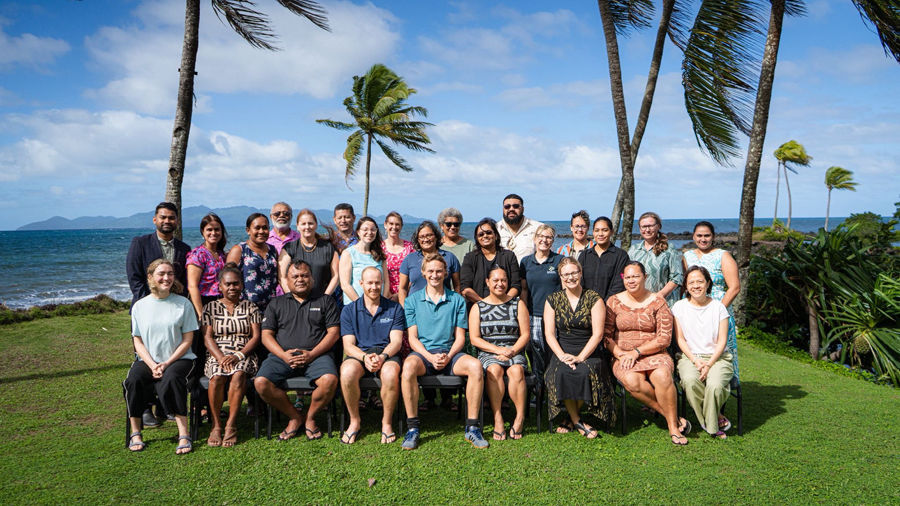 Group photo of workshop participants in front of palm trees and the ocean.