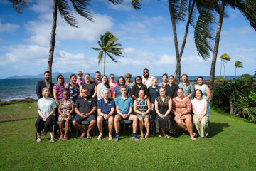 Group photo of workshop participants in front of palm trees and the ocean.