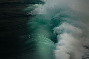 An aerial shot of a large wave crashing on to the ocean's surface causing whitewash.